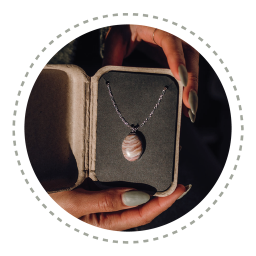 A woman holds an open kraft gift box with a beautiful striped stone pendant necklace inside