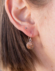 Close-up of an ear wearing a round dangle earring set with a chunk of natural red granite