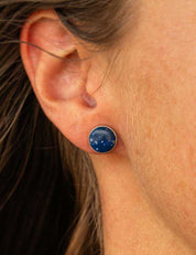 Close-up of an ear wearing a blue lapis lazuli stud earring with a sterling silver setting