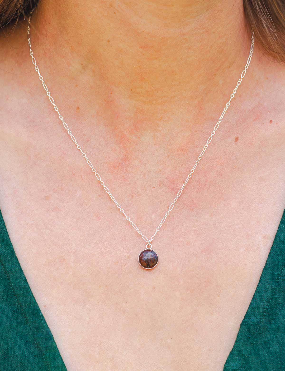 Dainty stone pendant necklace made from a natural rock worn by a woman, close-up view