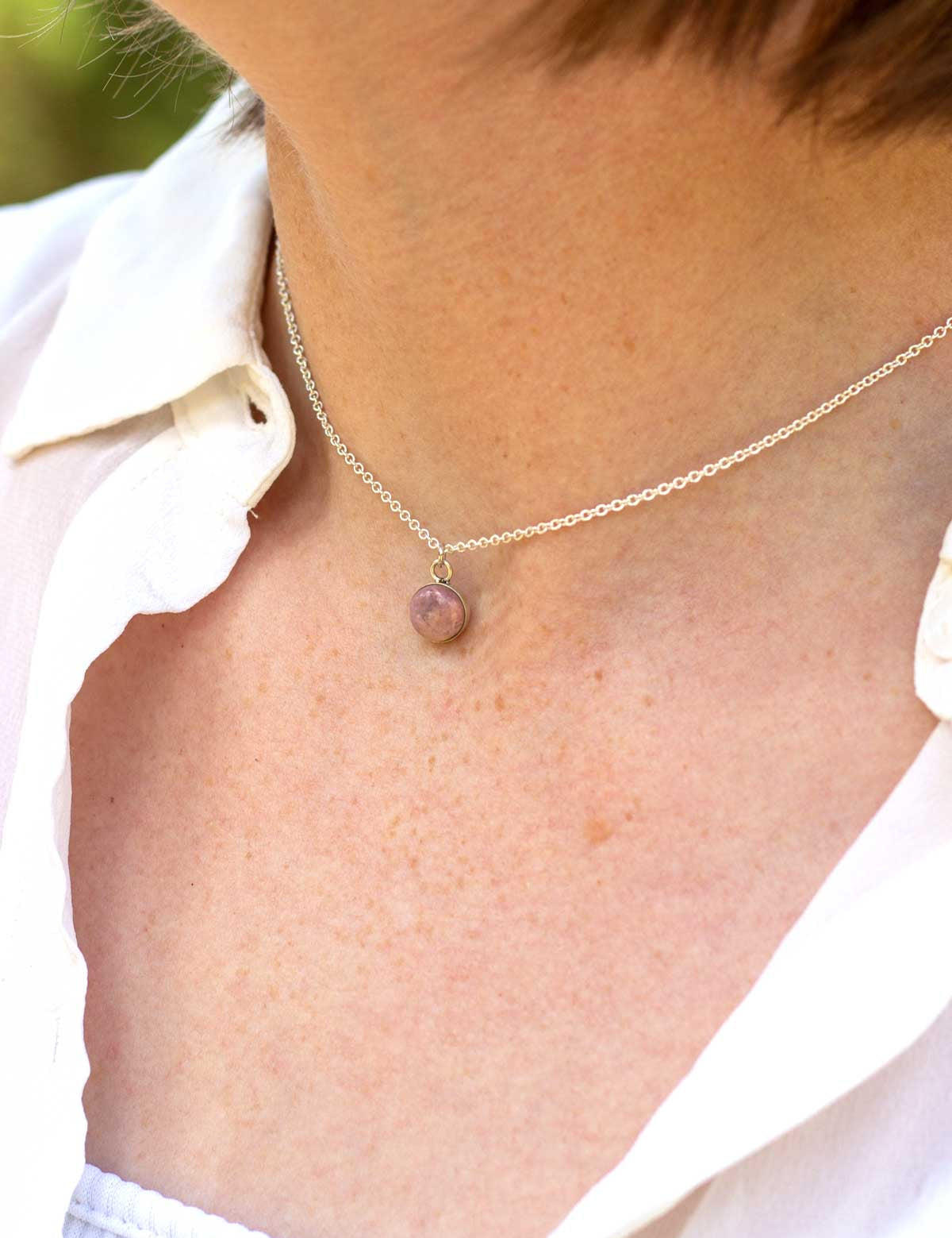 Choker length pendant necklace made from a natural pink stone, worn by a person in a white oxford shirt