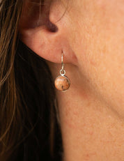 Close-up of an ear wearing a round dangle earring set with pink granite