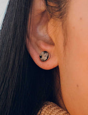 Close-up of an ear wearing a round stud earring set with natural granite