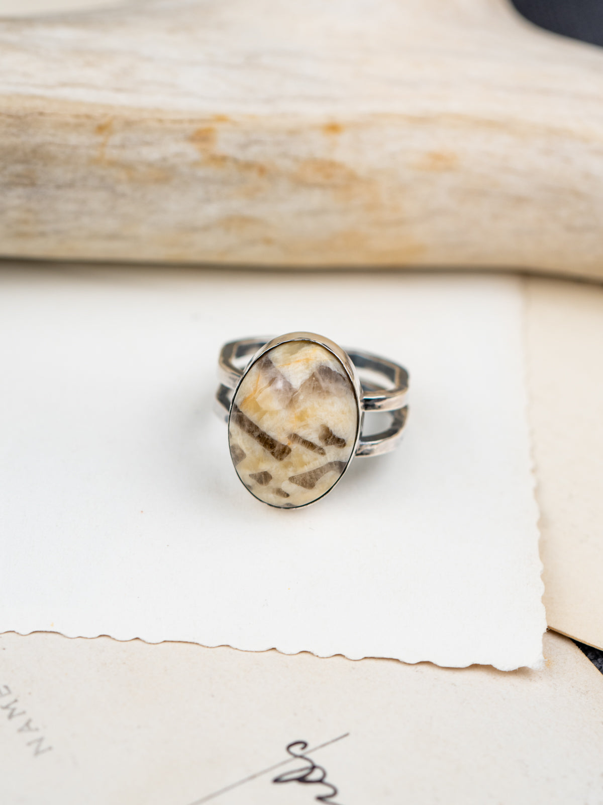 Zebra stone statement ring with a polished oval stone featuring natural brown and cream striations, set in a handcrafted metal bezel with a double-banded shank. Placed on postcards.