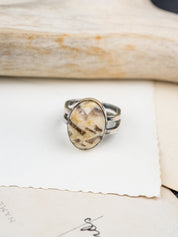 Zebra stone statement ring with a polished oval stone featuring natural brown and cream striations, set in a handcrafted metal bezel with a double-banded shank. Placed on postcards.