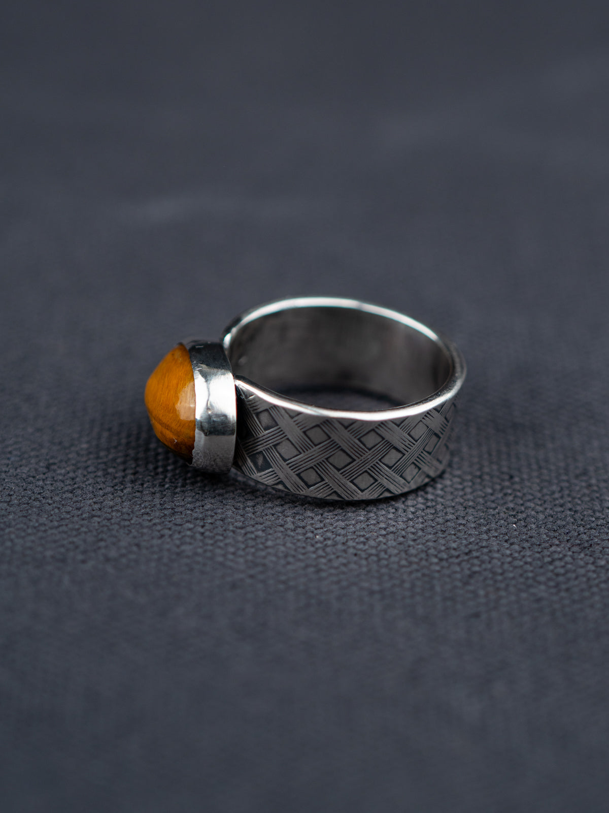 Side profile of a Tiger eye stone ring with a polished oval gemstone set in a textured metal band, showcased on dark fabric background.