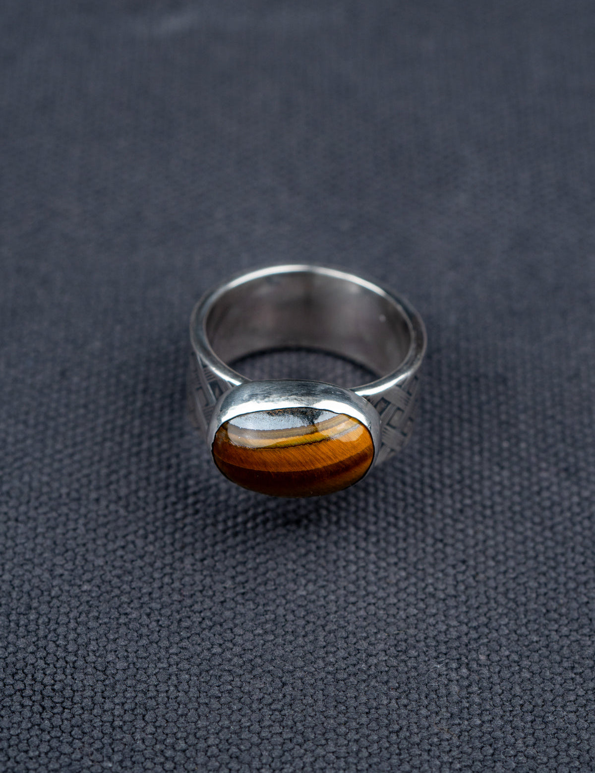 Tiger eye stone ring with a polished oval gemstone set in a textured metal band, showcased on dark fabric background.