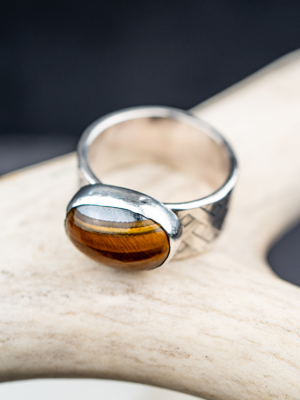 Tiger eye stone ring with a polished oval gemstone set in a textured metal band, showcased on a cream colored antler.