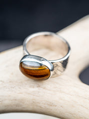 Tiger eye stone ring with a polished oval gemstone set in a textured metal band, showcased on a cream colored antler.