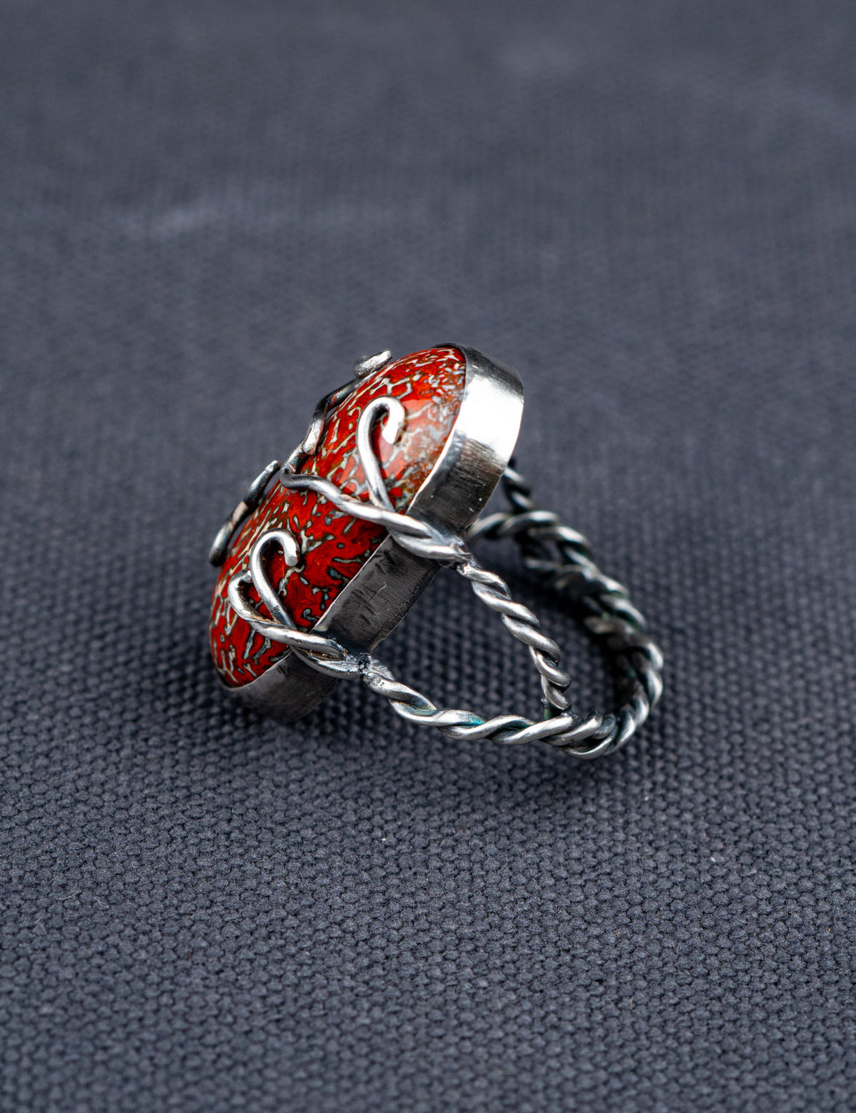 Side profile of a Dinosaur bone stone ring featuring a patterned fossilized gemstone set in a metal bezel with a twisted band, displayed on dark textured fabric.
