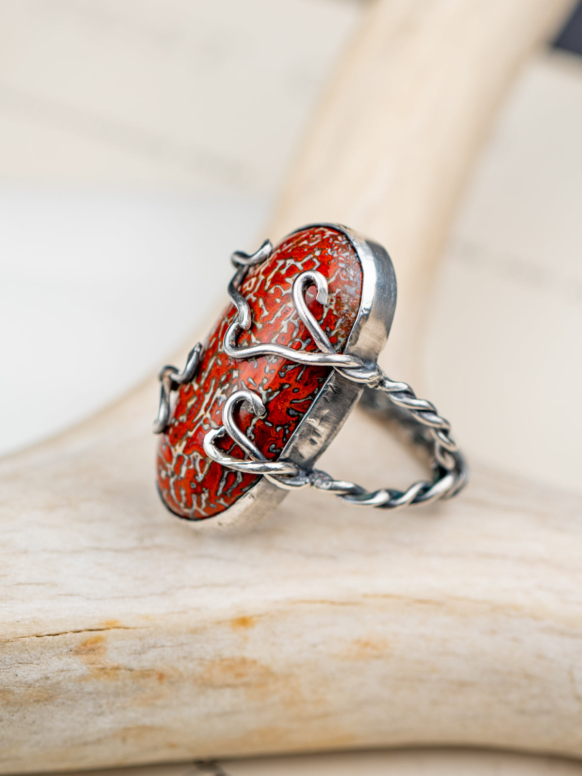 Dinosaur bone stone ring featuring a patterned fossilized gemstone set in a metal bezel with a twisted band, displayed on a cream colored antler.