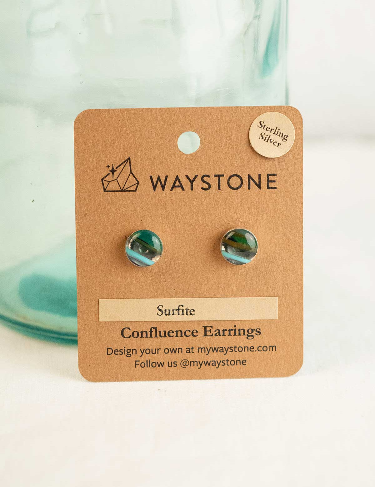 Waystone surfite confluence earrings on a kraft jewelry card with a glass container in the background.
