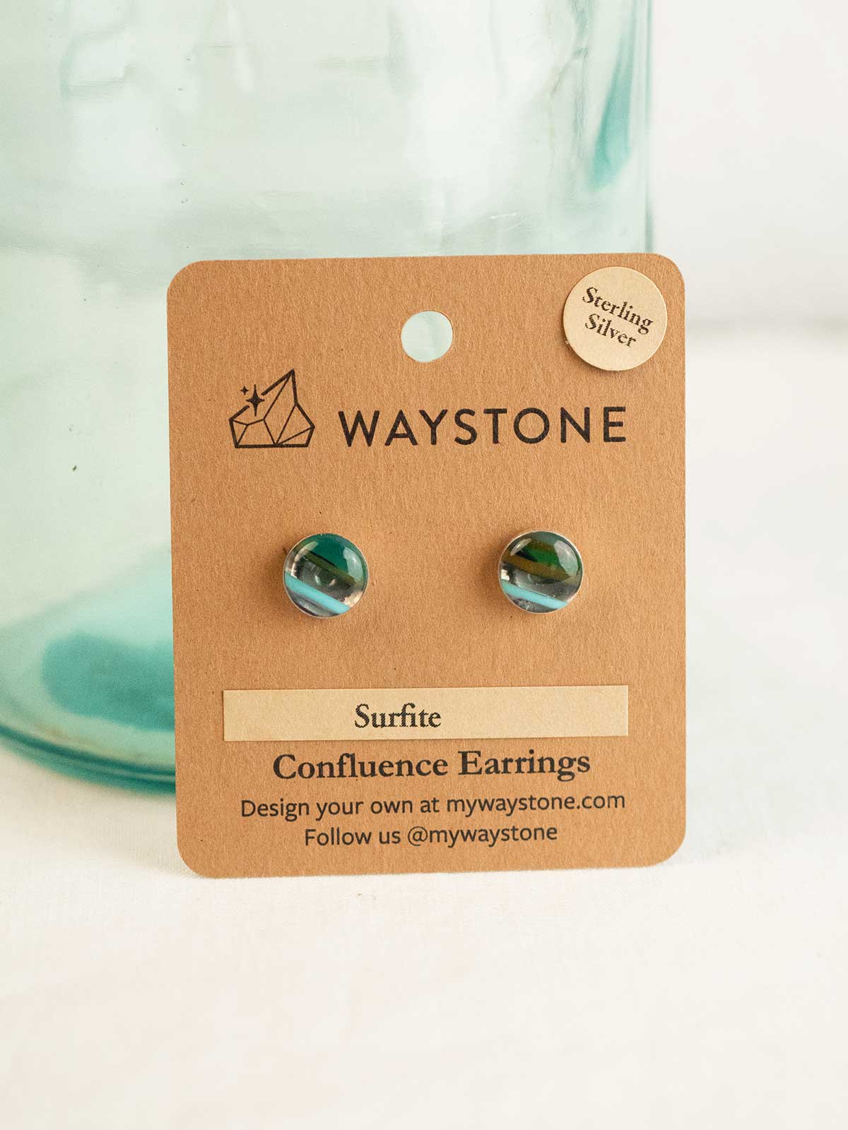 Waystone surfite confluence earrings on a kraft jewelry card with a glass container in the background.
