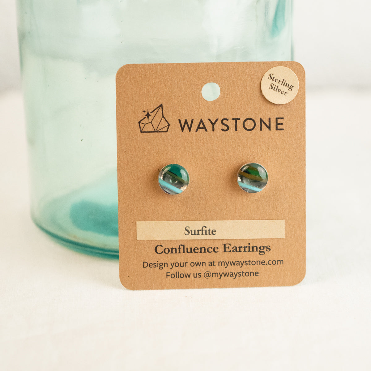 Waystone surfite confluence earrings on a kraft jewelry card with a glass container in the background.