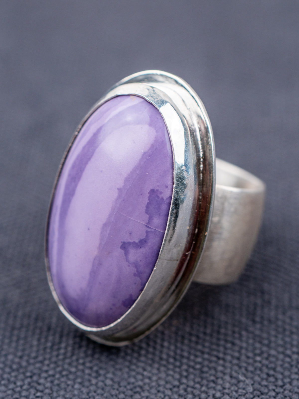 Sterling silver ring featuring a Tiffany stone with natural purple tones, photographed on a textured gray fabric background.