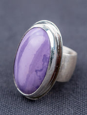 Sterling silver ring featuring a Tiffany stone with natural purple tones, photographed on a textured gray fabric background.