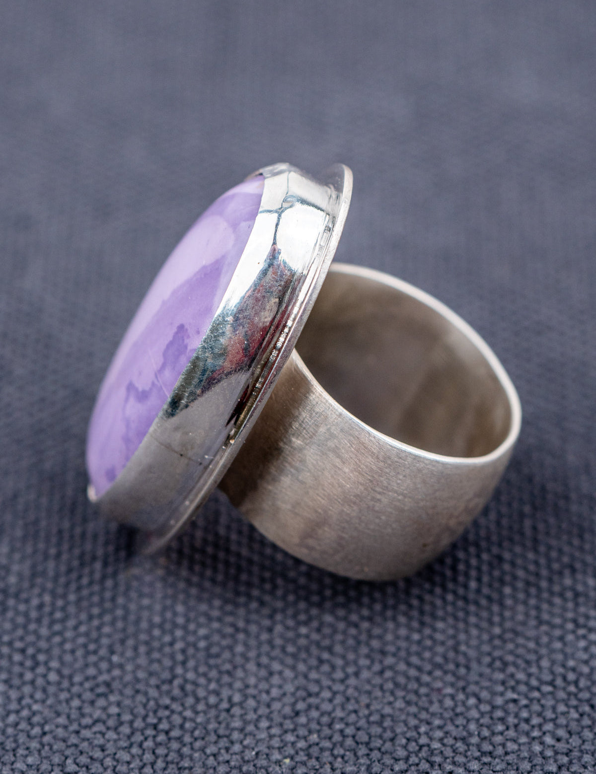 Sterling silver ring featuring a Tiffany stone with natural purple tones, photographed from the side on a gray background