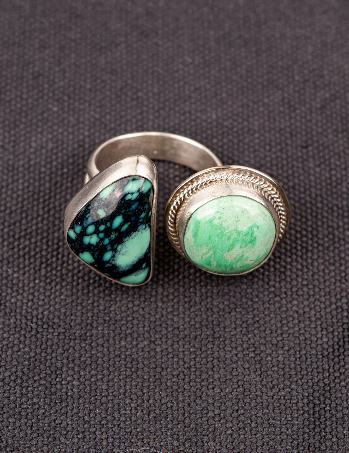 Open silver ring featuring a variscite stone with greenish-blue hues set in an open bezel design, displayed on a dark fabric background.