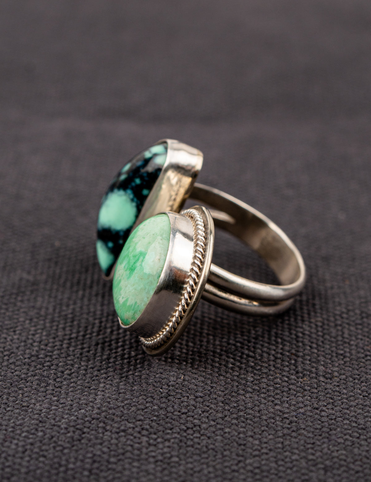 Side profile of a open silver ring featuring a variscite stone with greenish-blue hues set in an open bezel design, displayed on a dark fabric background.