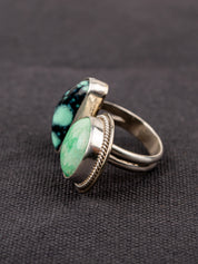 Side profile of a open silver ring featuring a variscite stone with greenish-blue hues set in an open bezel design, displayed on a dark fabric background.
