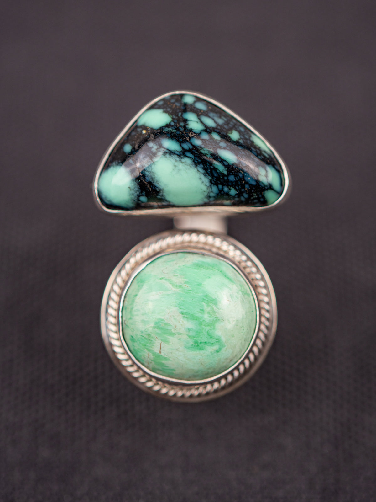 Up-close open silver ring featuring a variscite stone with greenish-blue hues set in an open bezel design, displayed on a dark fabric background.