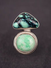 Up-close open silver ring featuring a variscite stone with greenish-blue hues set in an open bezel design, displayed on a dark fabric background.