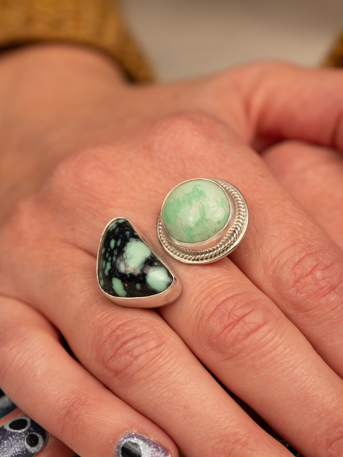 Open silver ring featuring a variscite stone with greenish-blue hues set in an open bezel design, displayed on a person's middle finger
