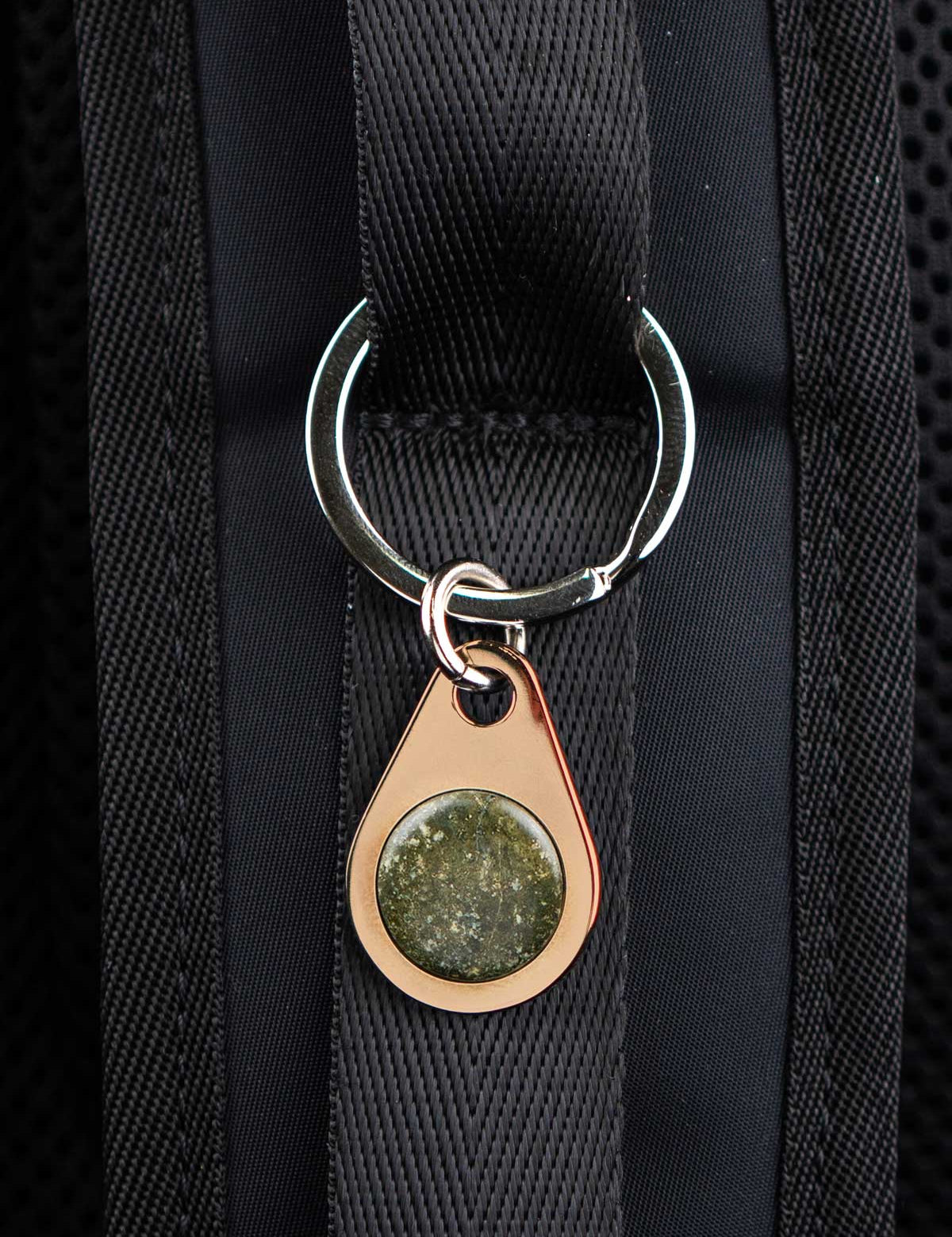 Champagne color metal keychain tag set with a custom green stone on a black bag