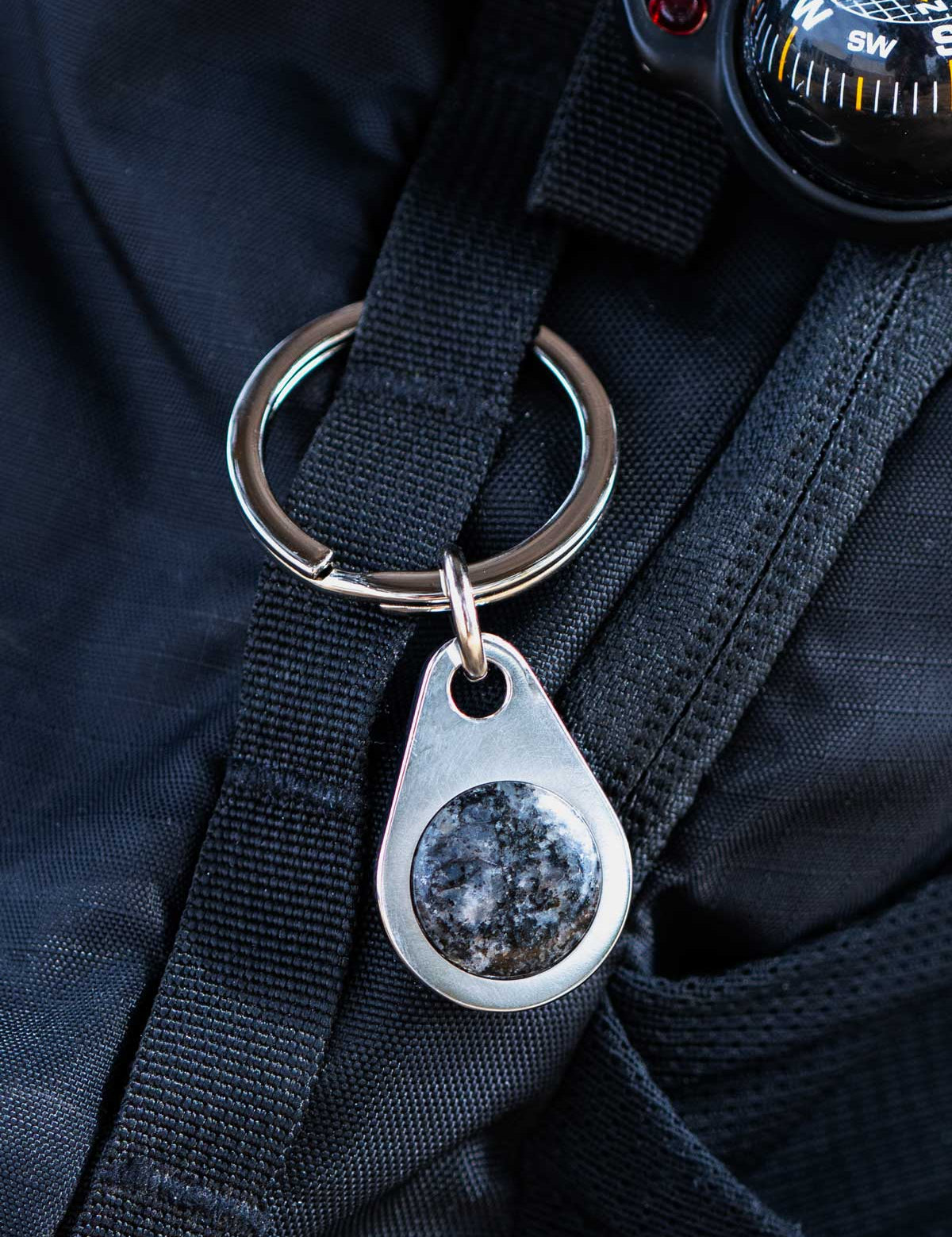 Keychain with a stone pendant set into a metal key tag, attached to a black backpack with a compass