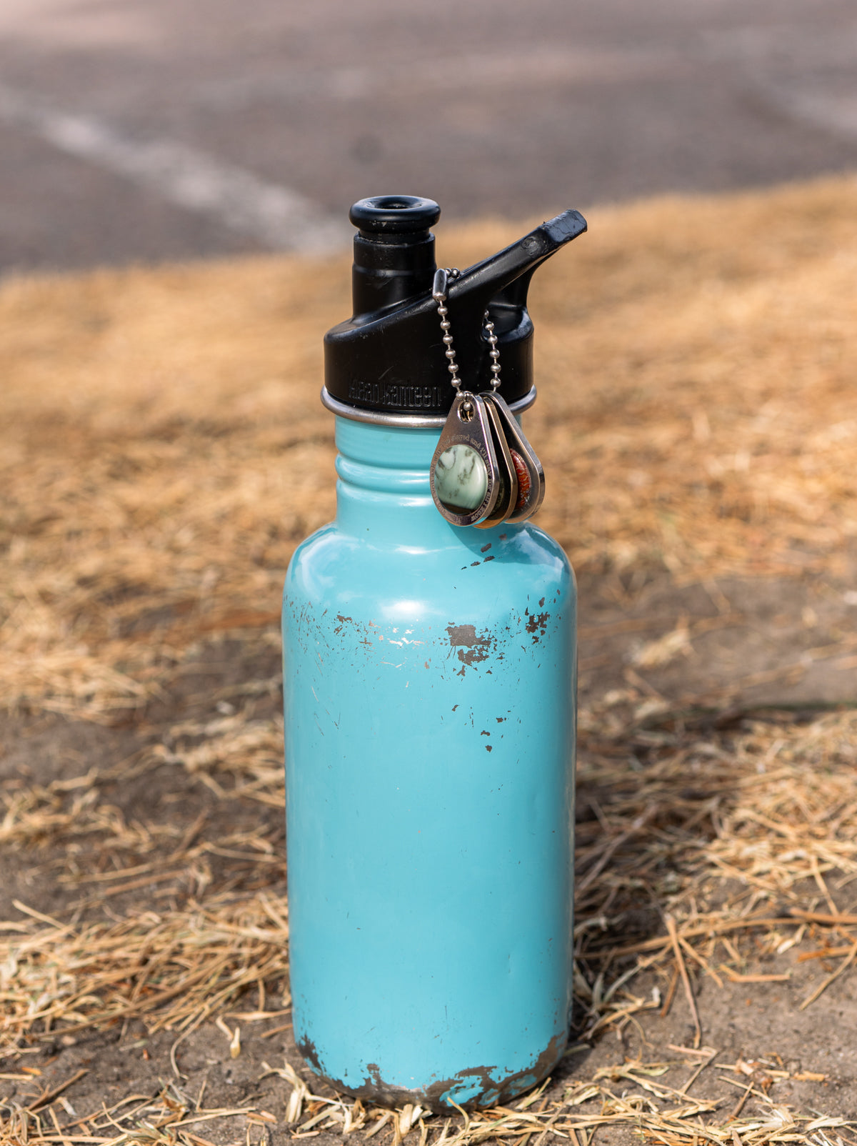 Blue water bottle sitting outside with a set of 3 custom zipper pull tags adorned with round stones and personalized engraving