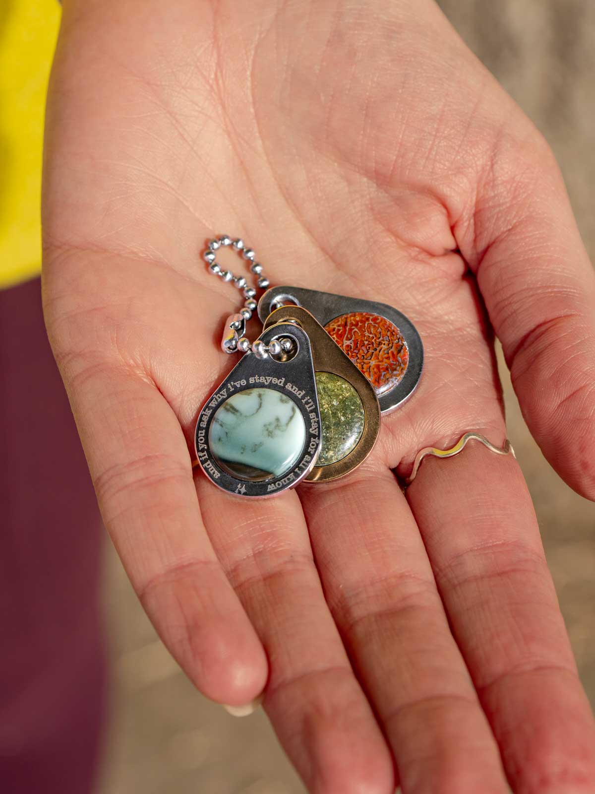 Three small stone and metal zipper pull tags on a ball chain held in a hand
