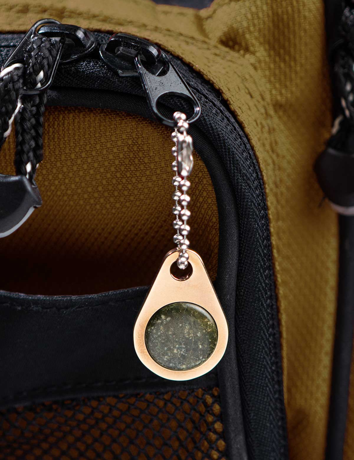 Close-up of a champagne color metal zipper pull tag with a green stone on a backpack