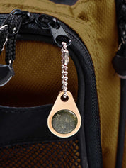 Close-up of a champagne color metal zipper pull tag with a green stone on a backpack