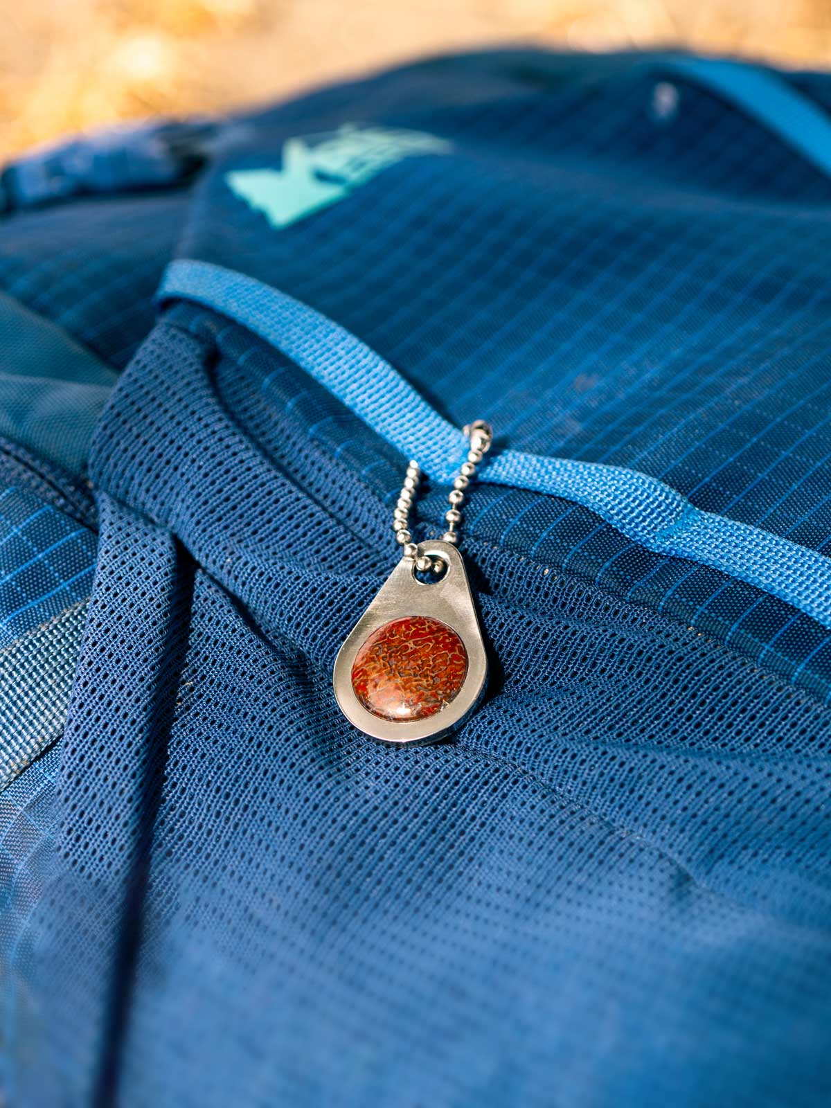 A blue REI backpack with a custom stone zipper pull tag on a ball chain 