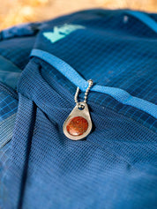 A blue REI backpack with a custom stone zipper pull tag on a ball chain 