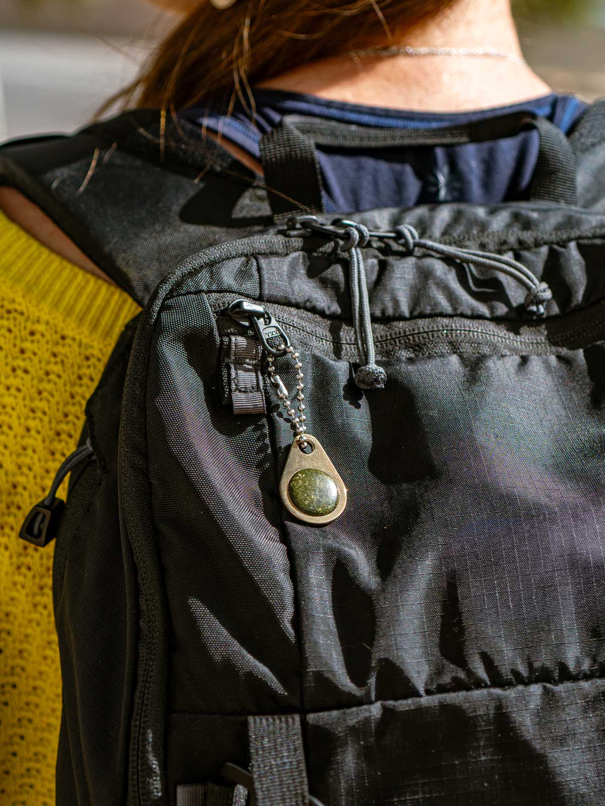 Person wearing a black backpack with a custom zipper pull attached that's been custom made with a natural green stone