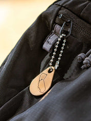 Ball chain custom zipper pull with a metal tag personalized with an engraving of the state of California and attached to a black backpack