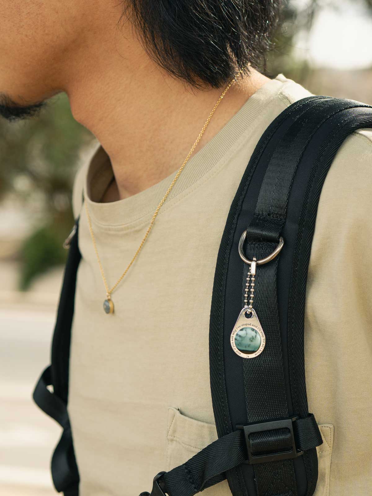Person wearing a black backpack with a custom engraved stone zipper pull, outdoors.