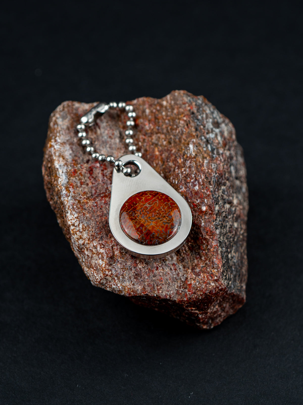 Teardrop-shaped zipper pull on a ball chain set with a red stone and sitting on the customer's original rock it was made from