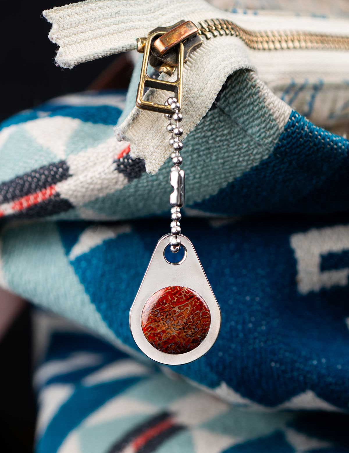 Teardrop-shaped custom zipper pull with a red stone on a blue and white patterned bag