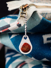 Teardrop-shaped custom zipper pull with a red stone on a blue and white patterned bag