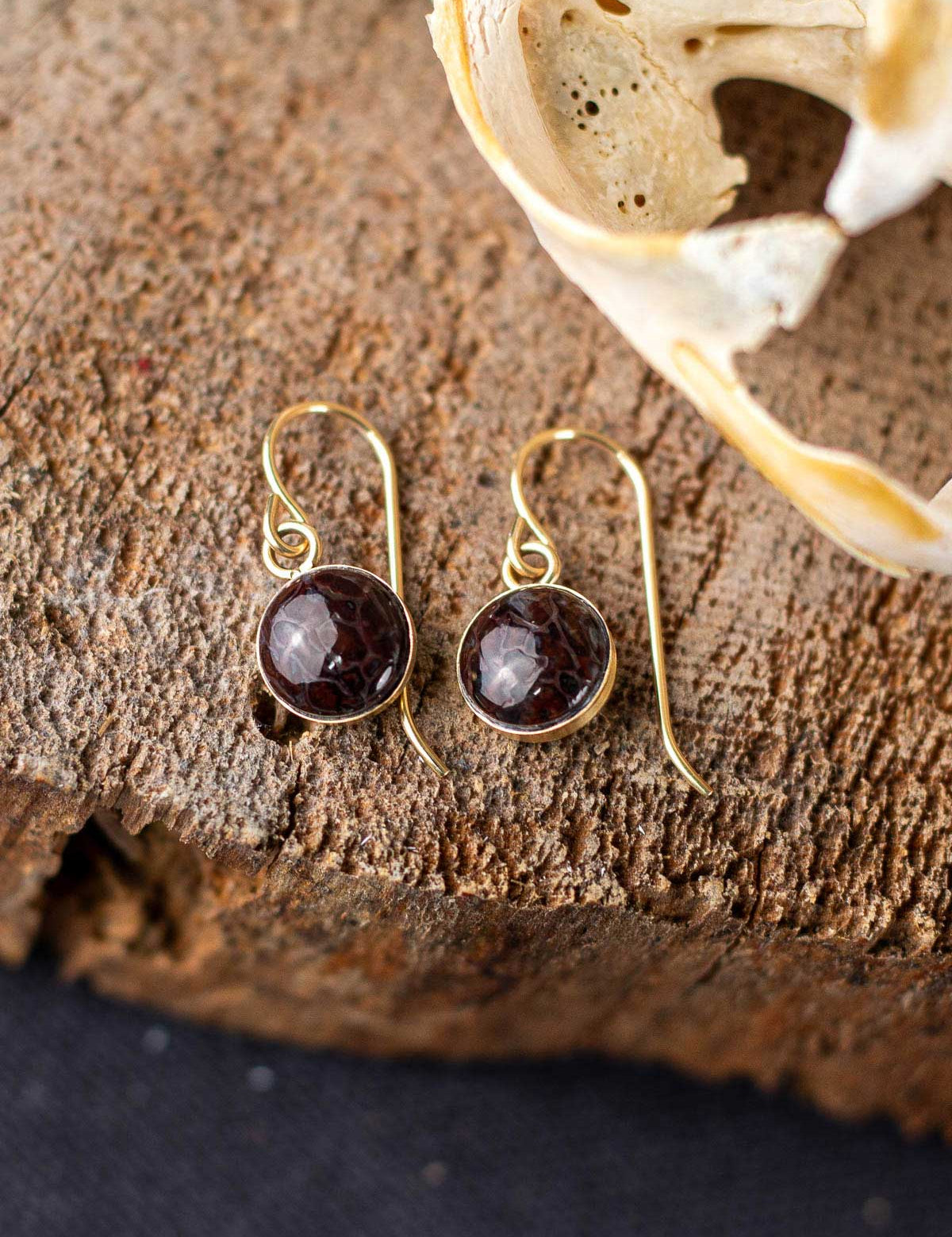 Dangling red fossilized dinosaur gembone earrings with a gold ear wire and backing