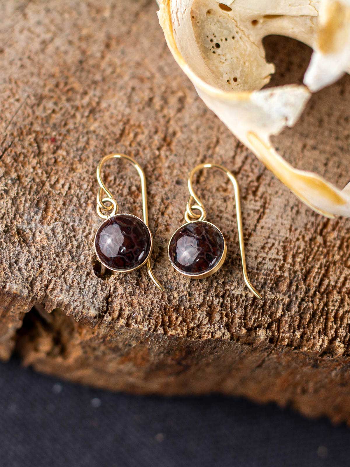 Dangling red fossilized dinosaur gembone earrings with a gold ear wire and backing