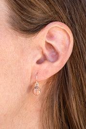 Close-up of an ear wearing a dangling earring set with natural pink granite