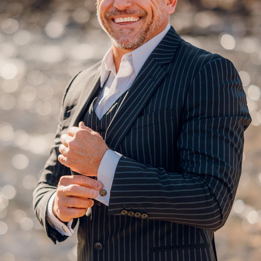 A man in a pinstripe suit smiles while wearing a custom cufflink made of raw cement