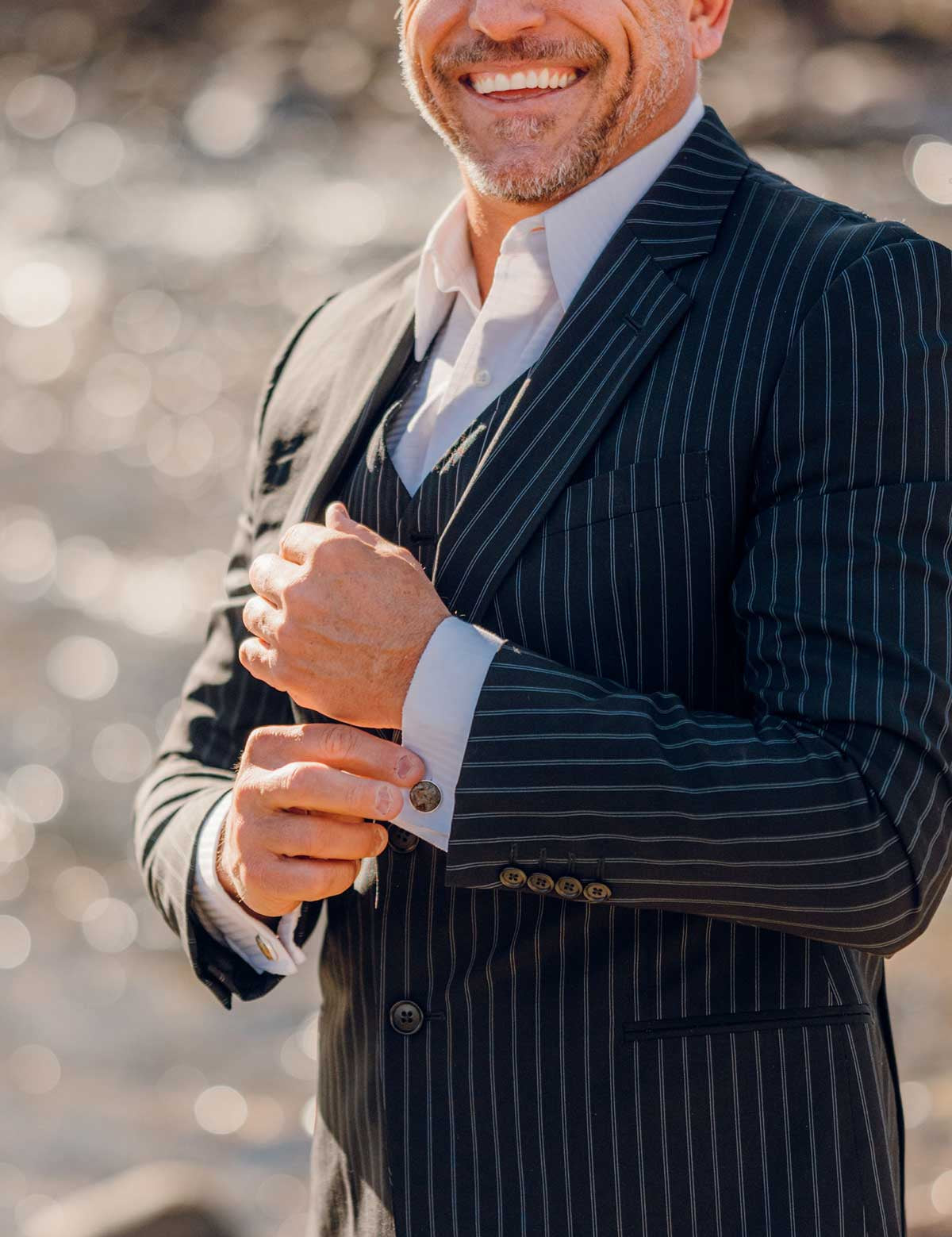 A man in a pinstripe suit smiles while wearing a custom cufflink made of raw cement