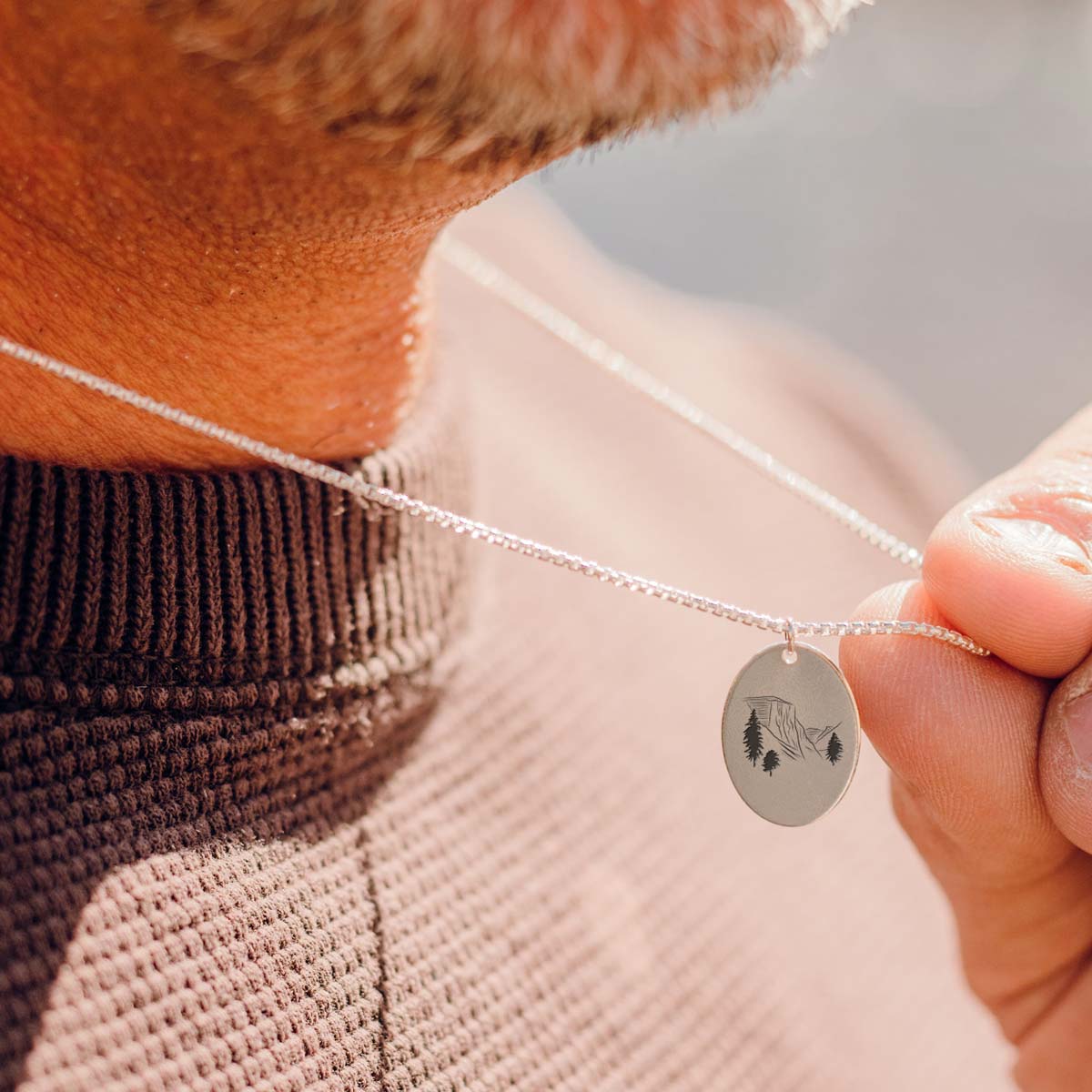 A man wears a sterling silver charm necklace engraved with a mountain peak