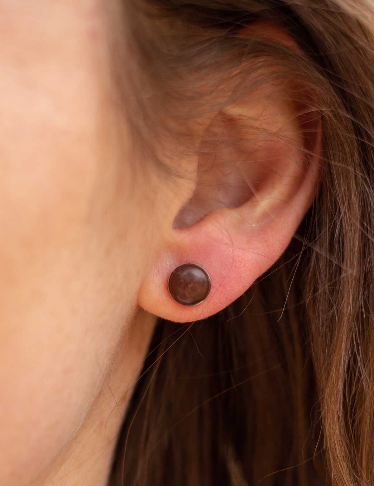Woman wears small round stone earrings made of reddish-brown rock