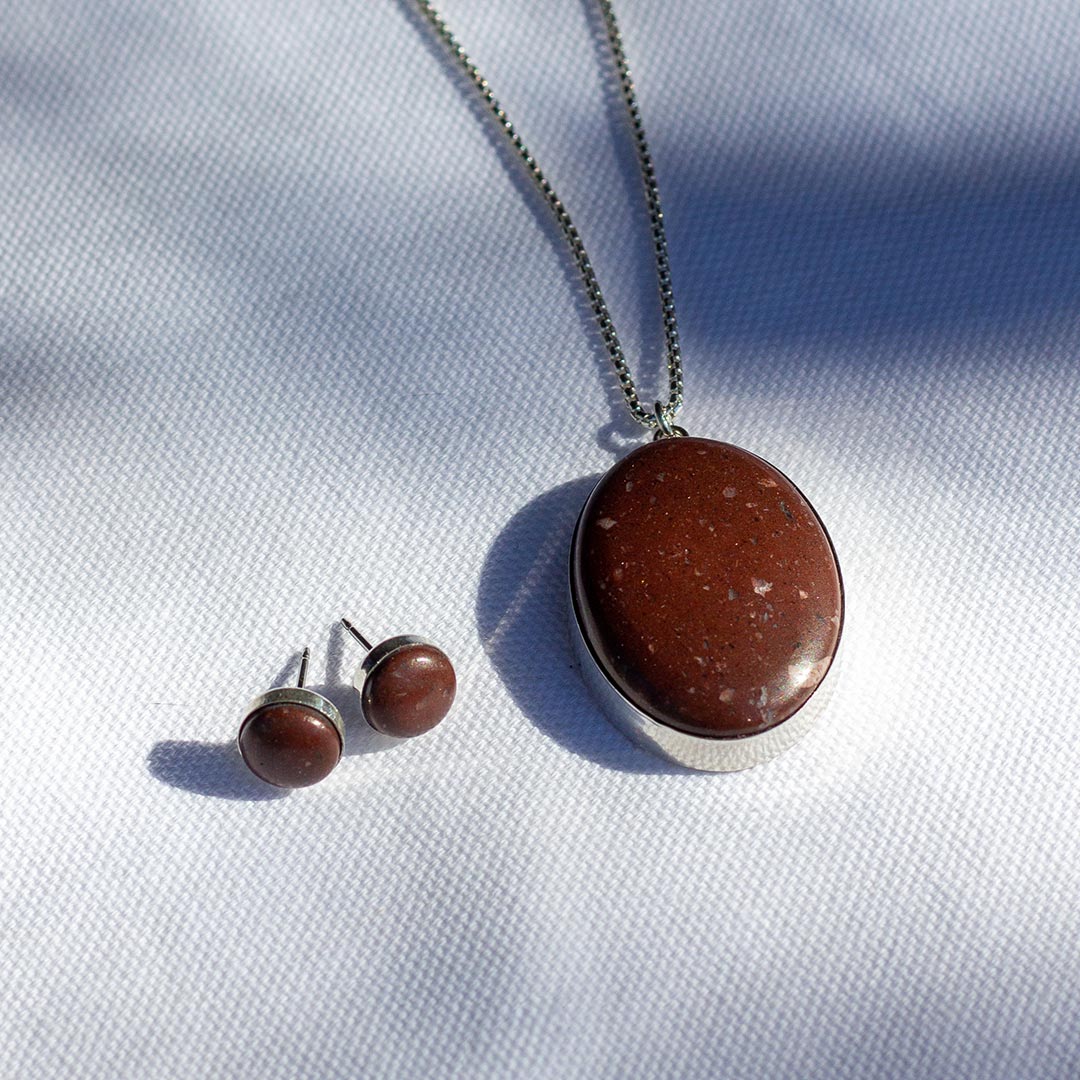 A custom jewelry set with small stud earrings and a large pendant necklace made of the same reddish-brown stone