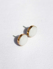 A pair of white stud earrings with a stone set in a 14k gold fill cup. The edge is personalized with custom engraving.
